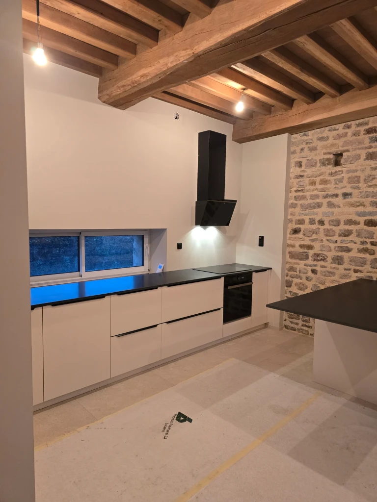 Cuisine réalisée par Bastien De Almeida : façades claires, plan de travail sombre et mur en pierre